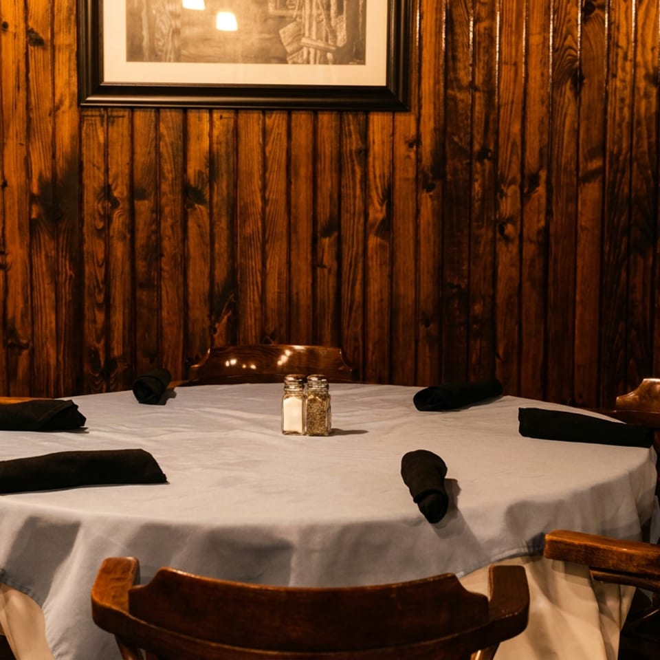 Round dining table with white tablecloth, black napkins, salt and pepper shakers, and wooden chairs.